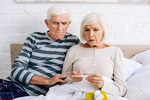 Sad husband and wife looking at thermometer in apartment — Stock Photo
