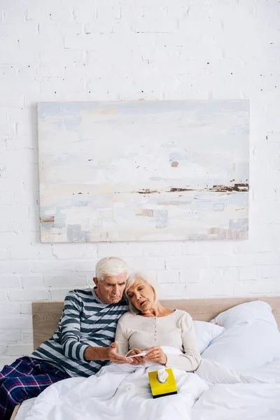 Marido y mujer guapos mirando termómetro en el apartamento - foto de stock