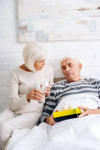 Wife giving glass of water to ill husband in bed — Stock Photo