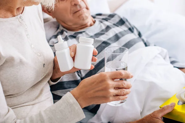 Vue recadrée de la femme donnant un verre d'eau au mari malade et tenant des pilules — Photo de stock