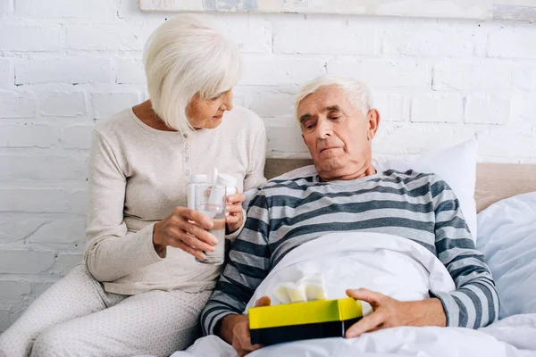Жена дает стакан воды больному мужу в постели — стоковое фото