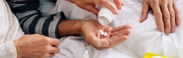 Tiro panorámico de la esposa dando pastillas a marido enfermo - foto de stock