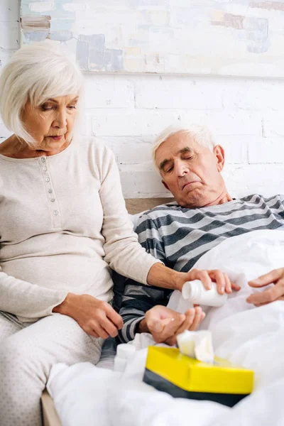 Femme aînée donnant des pilules au mari malade au lit — Photo de stock