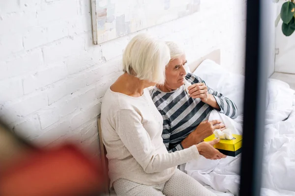 Vista ad alto angolo del marito utilizzando gocce nasali e moglie che tiene i tovaglioli in appartamento — Foto stock