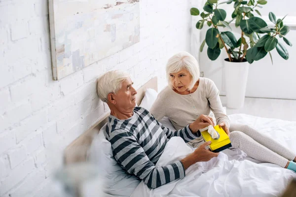 Высокий угол зрения жены давая салфетки больному мужу в постели — стоковое фото