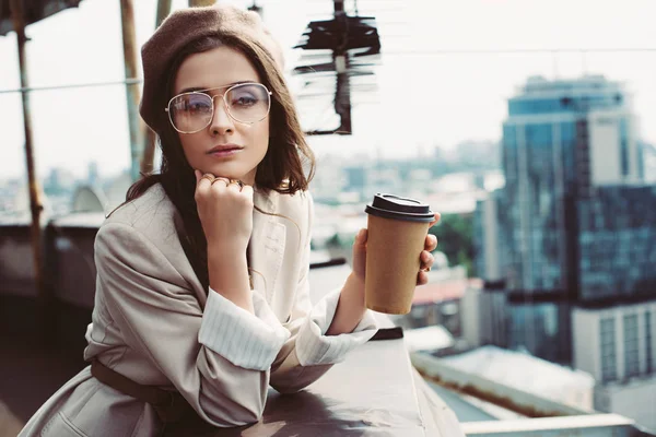Elegant pensive girl in beige suit and beret posing on roof with coffee to go — Stock Photo