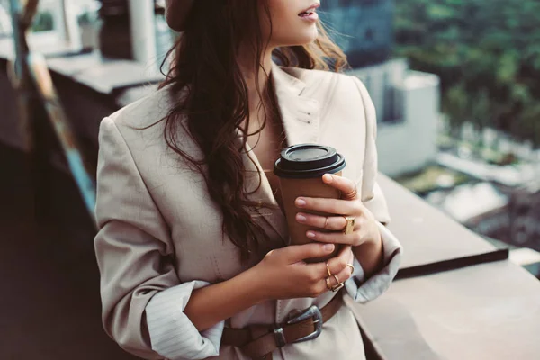 Обрезанный вид на модную девушку в бежевом костюме позирует на крыше с кофе, чтобы пойти — стоковое фото