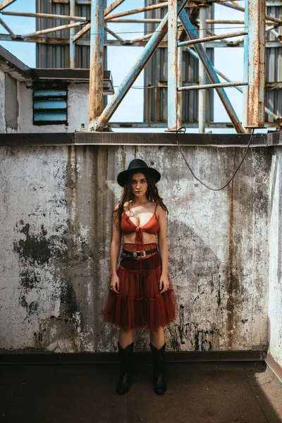 Attractive trendy girl posing in red skirt, bra and hat on roof — Stock Photo