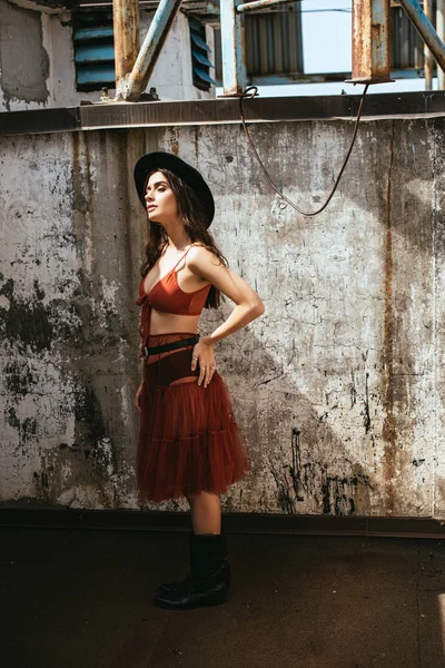 Attractive stylish girl posing in red skirt, bra and hat on roof — Stock Photo