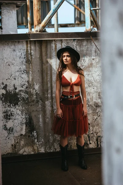 Atractiva chica de moda posando en falda roja, sujetador y sombrero en el techo - foto de stock