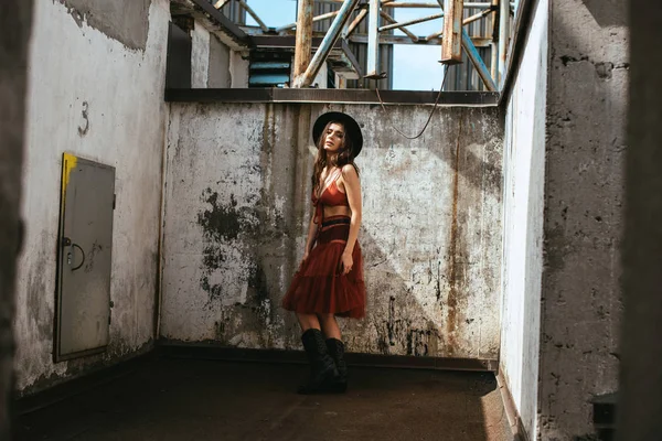 Hermosa mujer de moda posando en falda roja, sujetador y sombrero en el techo - foto de stock