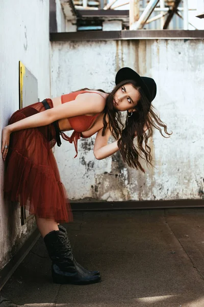 Модная девушка позирует в красной юбке, лифчике и шляпе на крыше — стоковое фото
