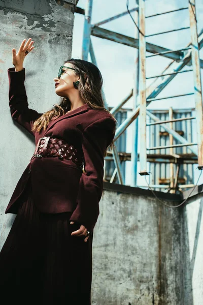Модна жінка позує в модному бордовому костюмі і сонцезахисних окулярах на міському даху — стокове фото