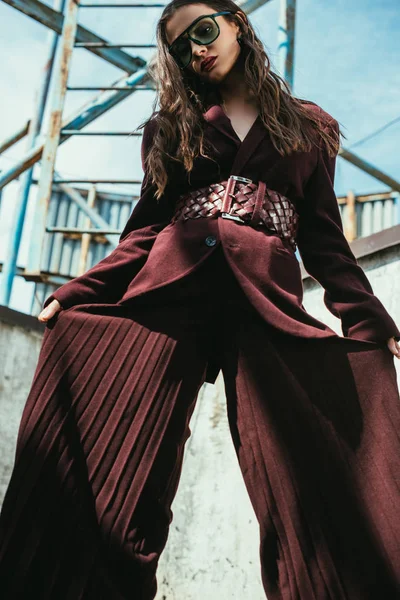 Элегантная модель в модном бордовом костюме и солнцезащитных очках на городской крыше — стоковое фото