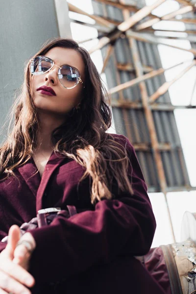 Beautiful girl posing in trendy burgundy suit and sunglasses on urban roof — Stock Photo