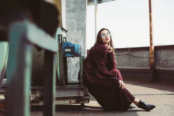 Menina elegante atraente posando em terno borgonha na moda e óculos de sol no telhado urbano — Fotografia de Stock