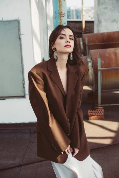 Hermosa chica elegante posando en vestido de seda y chaqueta marrón en el techo - foto de stock