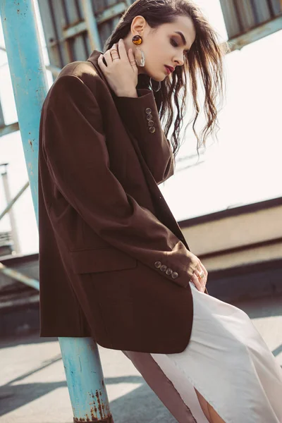 Chica elegante posando en vestido de seda y chaqueta marrón en el techo - foto de stock