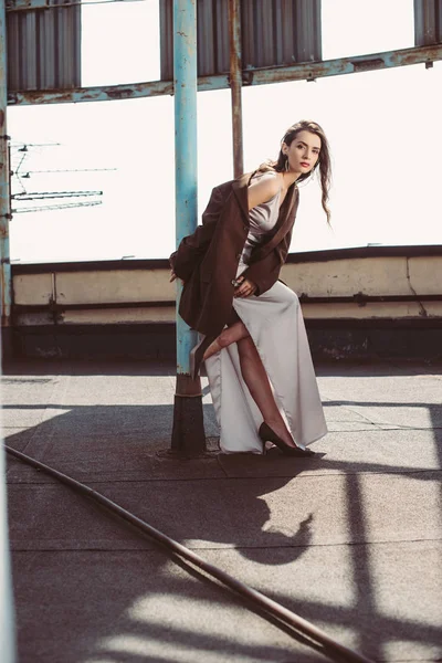 Модная элегантная девушка позирует в шелковом платье и коричневой куртке на крыше — стоковое фото