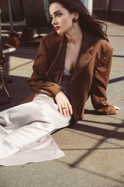 Hermosa mujer elegante posando en vestido de seda y chaqueta marrón en el techo - foto de stock