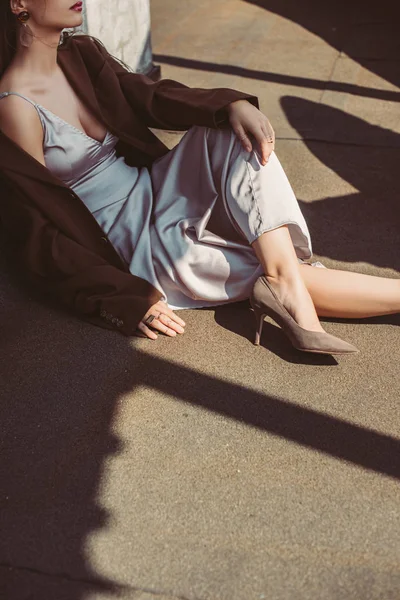 Vista recortada de la elegante mujer de moda posando en vestido de seda y chaqueta marrón en el techo - foto de stock