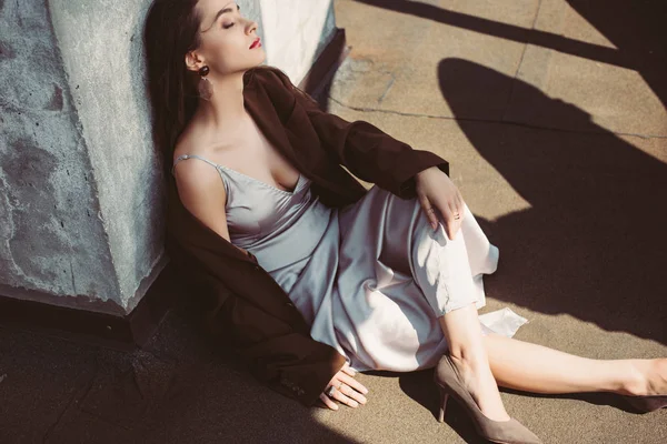 Fashionable elegant woman posing in silk dress and brown jacket on roof — Stock Photo