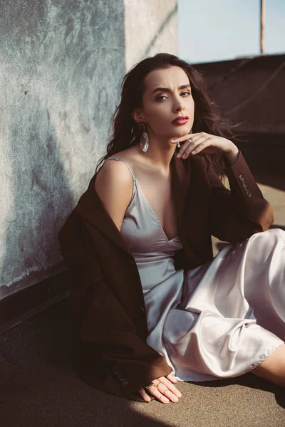 Stylish elegant woman posing in silk dress and brown jacket on roof — Stock Photo