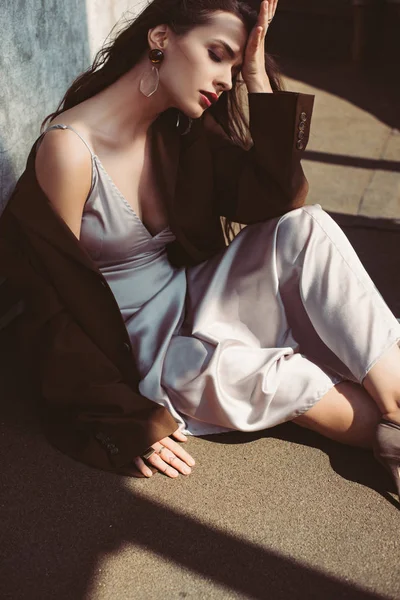 Atractiva mujer elegante posando en vestido de seda y chaqueta marrón en el techo - foto de stock