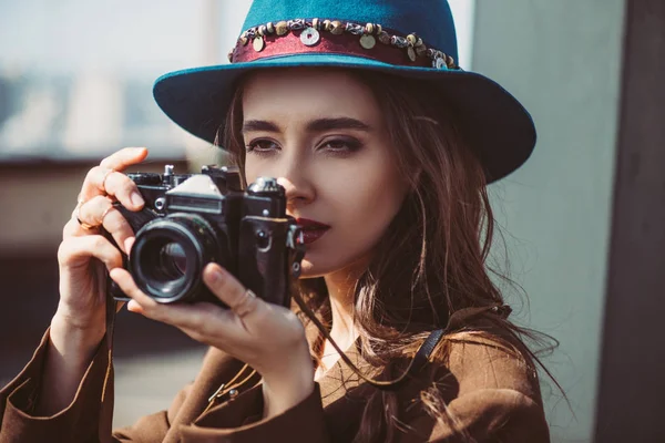 Elegant woman in hat taking photos on retro photo camera on roof — Stock Photo
