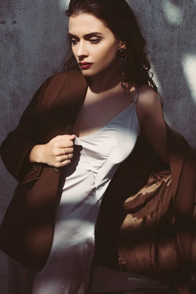 Elegant trendy model posing in silk dress and brown jacket on roof — Stock Photo