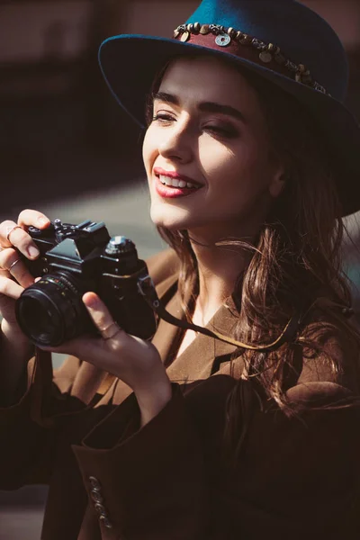 Mujer sonriente en sombrero tomando fotos en la cámara de fotos vintage en el techo - foto de stock