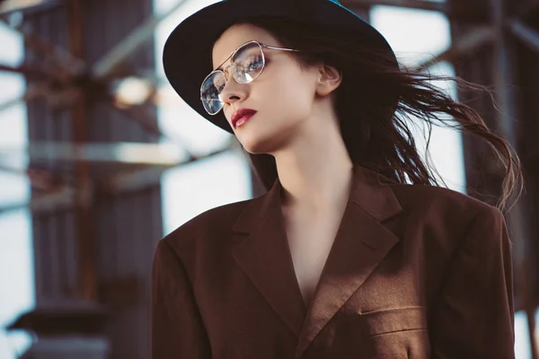 Stylish elegant woman posing in hat, eyeglasses and brown jacket on roof — Stock Photo
