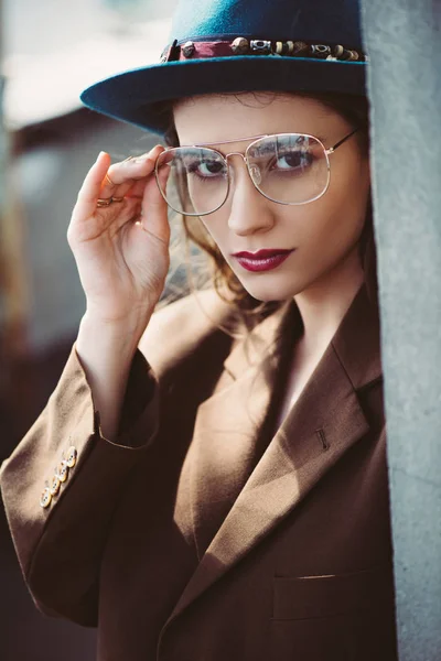 Mujer elegante de moda posando en sombrero, gafas y chaqueta marrón en el techo - foto de stock