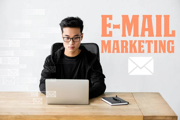 Asiático seo manager usando laptop y sentado cerca ilustración con e-mail marketing ilustración - foto de stock