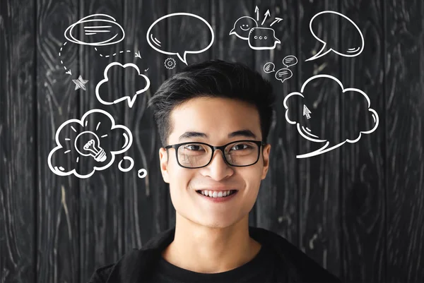 Sonriente asiático hombre en gafas mirando cámara en madera fondo con ilustración - foto de stock