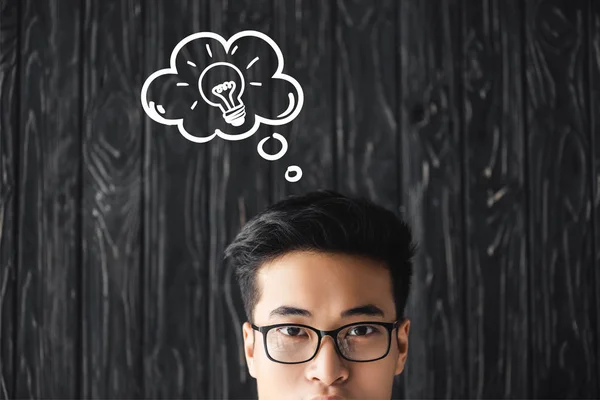 Recortado vista de asiático hombre en gafas mirando cámara en madera fondo con idea ilustración - foto de stock