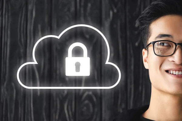 Cropped view of smiling asian hacker looking at illustration with padlock — Stock Photo