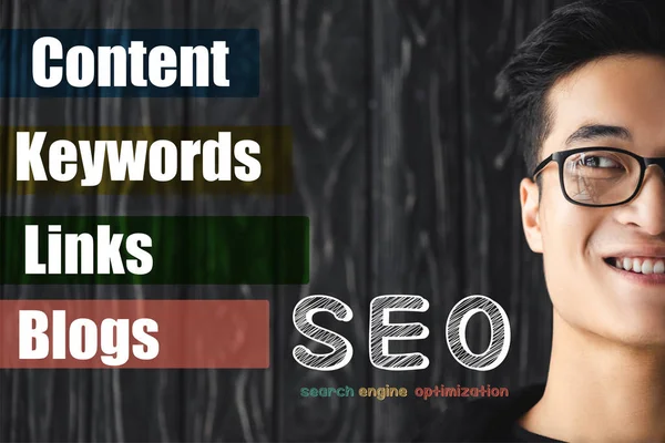 Cropped view of smiling asian seo manager looking at illustration with concept words of seo — Stock Photo