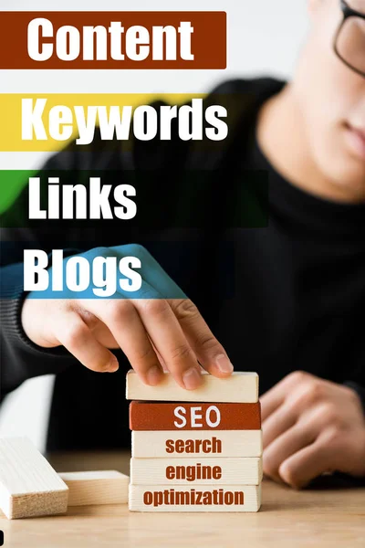 Selective focus of seo manager stacking wooden rectangles with lettering near illustration with keywords, links, blogs words — Stock Photo