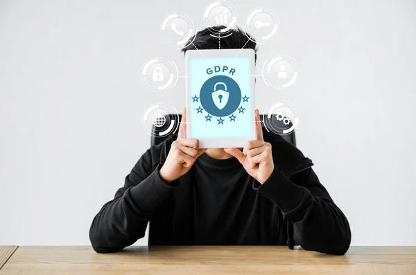 Hacker sitting at table and holding digital tablet with gdpr illustration — Stock Photo