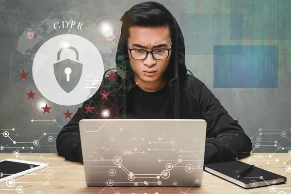 Hacker asiático usando el ordenador portátil y sentado cerca de candado ilustración y gdpr letras - foto de stock