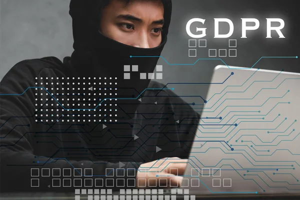 Hacker asiático usando el ordenador portátil y sentado cerca de ilustración gdpr - foto de stock