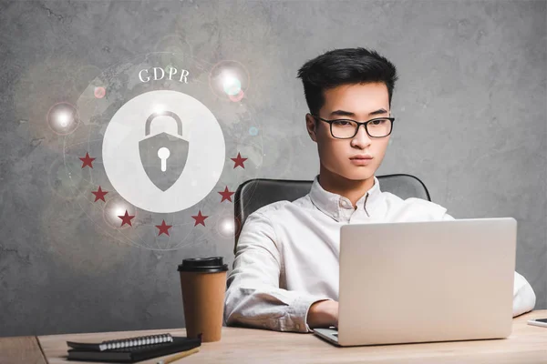 Asian businessman using laptop and sitting near padlock illustration and gdpr lettering — Stock Photo