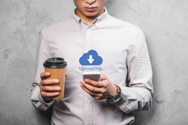 Cropped view of seo manager holding paper cup, using smartphone and standing near uploading illustration — Stock Photo