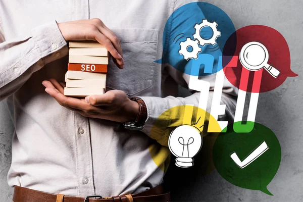 Cropped view of seo manager holding wooden rectangles and standing near seo illustration — Stock Photo