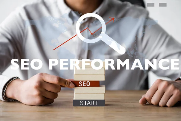 Cropped view of seo manager holding rectangle with seo lettering and sitting near seo performance illustration — Stock Photo