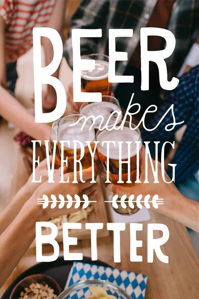 Vista recortada de amigos multiculturales tintinear vasos de cerveza ligera en el pub con cerveza hace todo mejor ilustración - foto de stock
