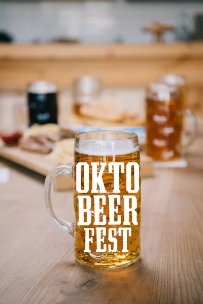 Selective focus of mug with lager beer and Oktobeerfest illustration on wooden table — Stock Photo