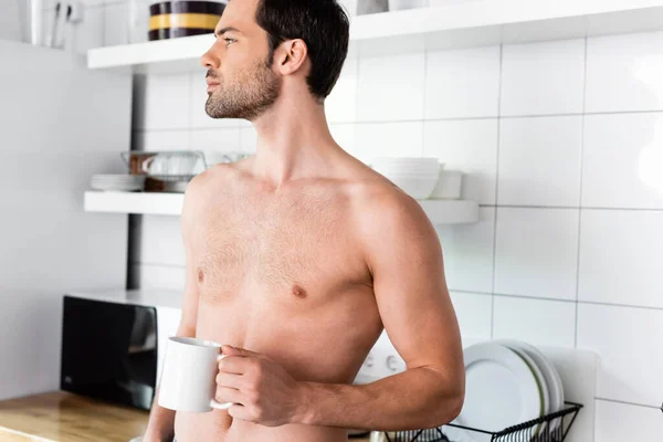 Homem sem camisa pensativo segurando xícara de café na cozinha em casa — Fotografia de Stock