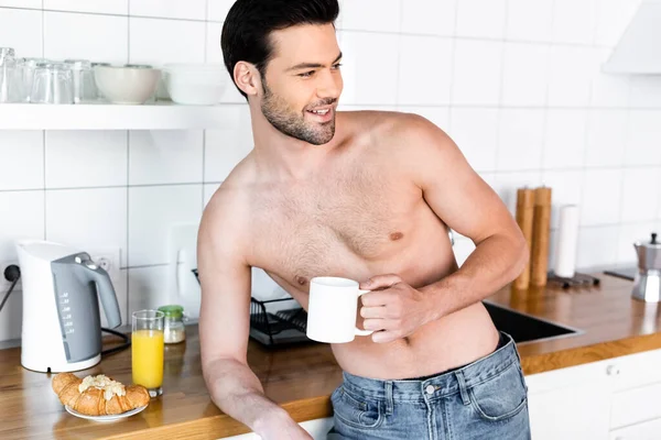 Cheerful shirtless man holding cup of coffee on kitchen with breakfast — Stock Photo